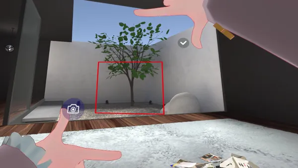 VR空間の中庭の木に向けて両手の指で四角を作り、赤い枠が表示され、左手の近くにカメラのボタンが浮かんでいる画面